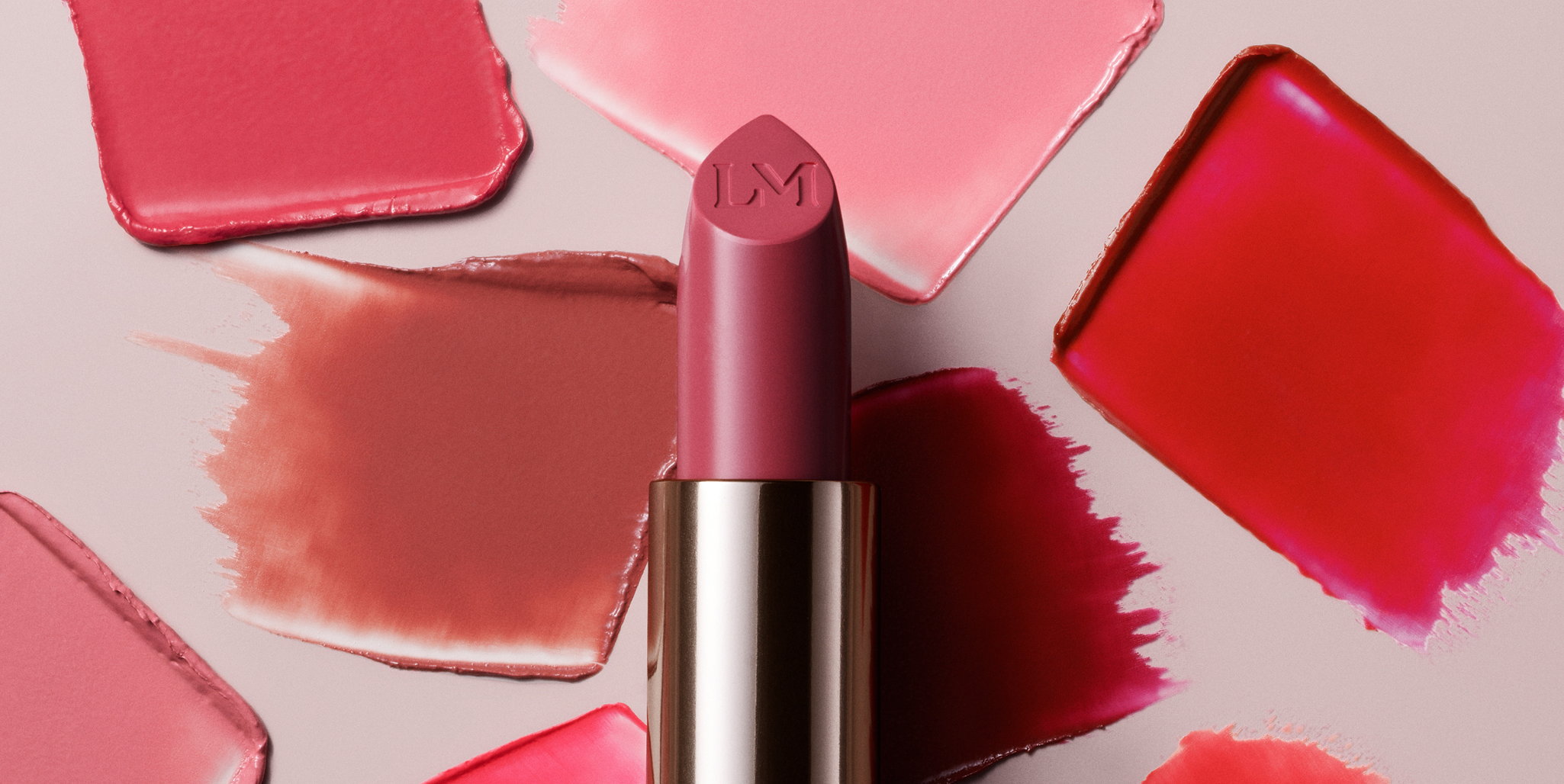 Stylized image of a deep pink shade of Laura Mercier Caviar Hydra-Creme lipstick with pink swatches in the background.