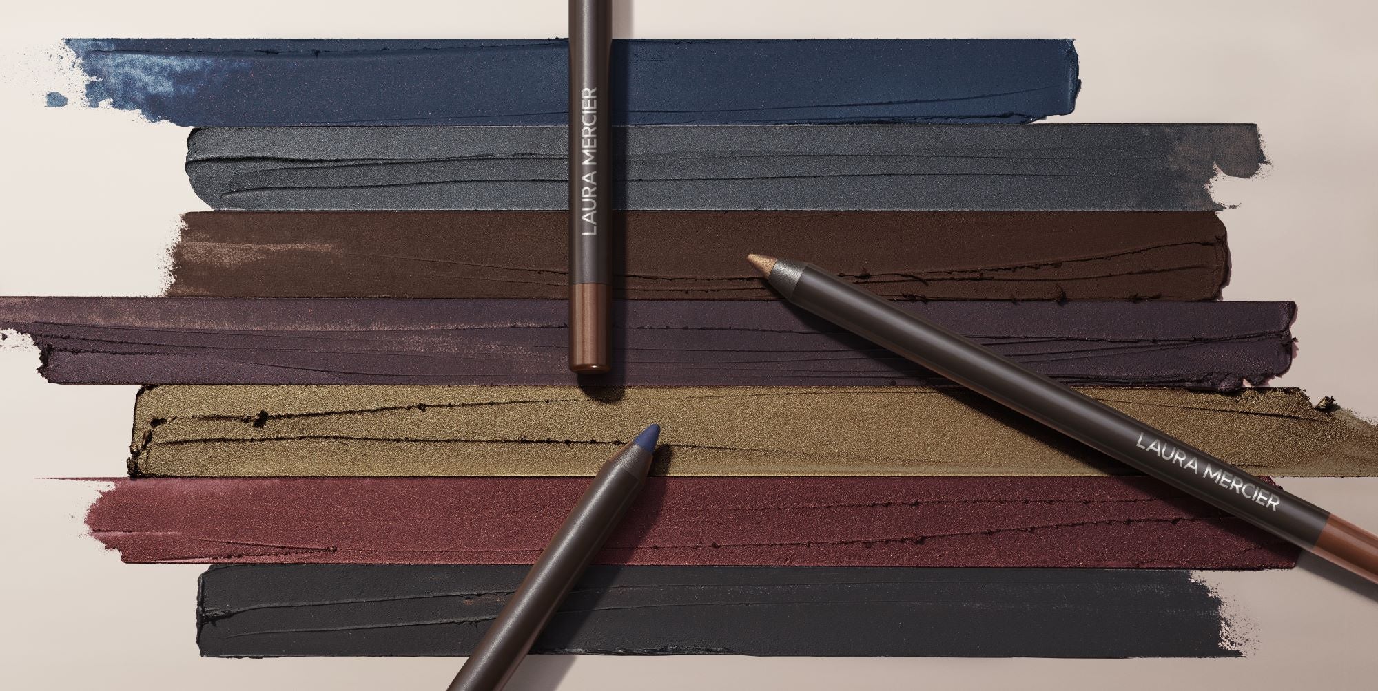 Laura Mercier Caviar eyeshadow sticks on top of a swatched background